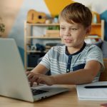 Young boy learning on a laptop at a desk.