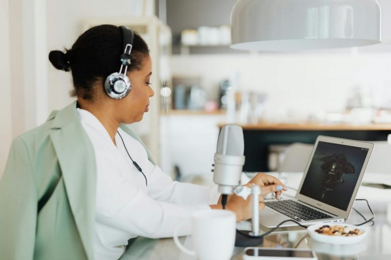 Woman using headphones and a microphone while working on a laptop indoors. Technology and lifestyle concept.
