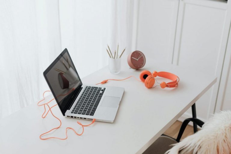 Minimalist workspace featuring a laptop and orange headphones on a clean white desk.