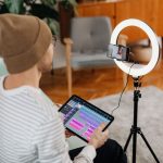 Man using a tablet for video recording with a ring light at home. Capturing digital content creatively.
